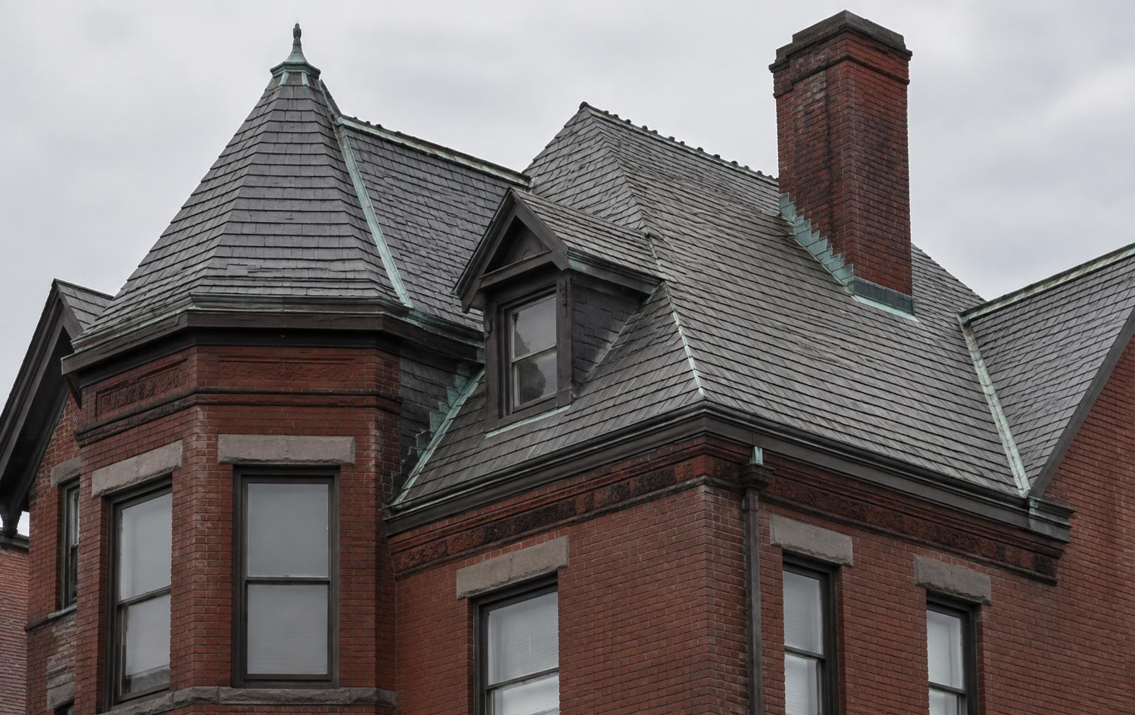 Steep natural slate roof with copper valley flashing on an older brick home